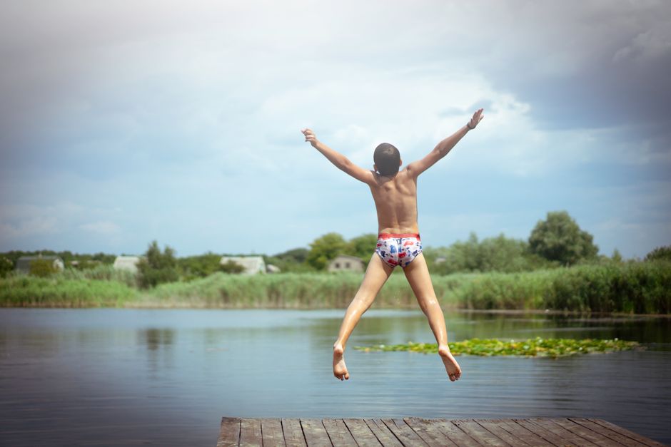 Young boy enjoying summer by jumping off a dock into a peaceful lake. Perfect example of carefree childhood leisure.