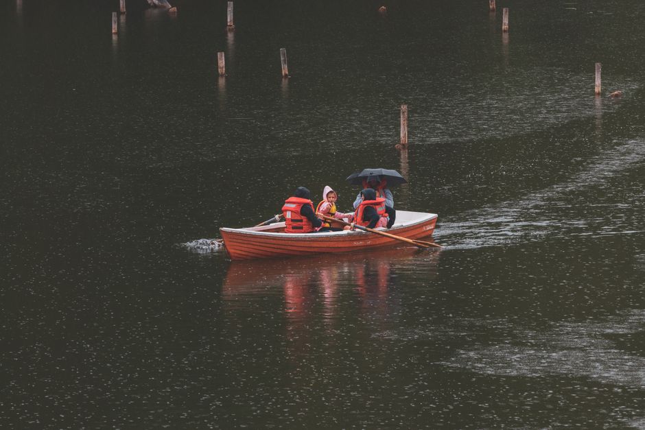 People in a rowboat with life vests, navigating a rainy lake scene.