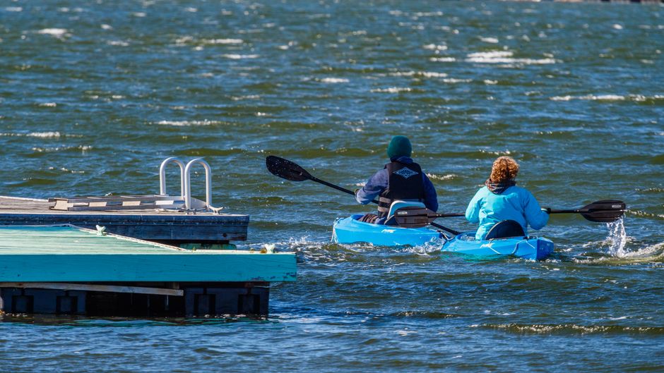 Two people kayaking on a sunny day near a dock, enjoying leisure time on the water.