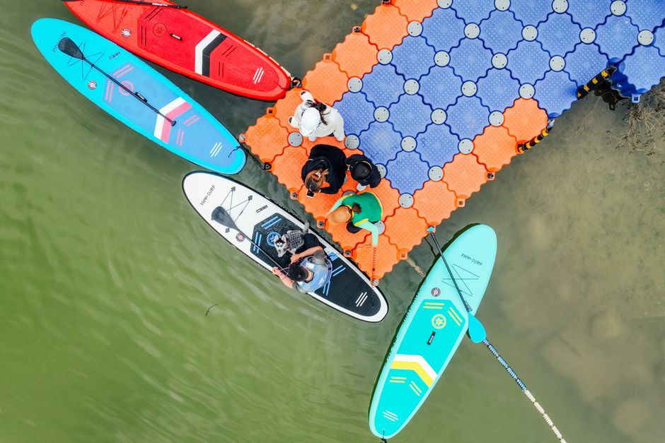 Top-down shot of paddleboards and people on a vibrant pier by the water.