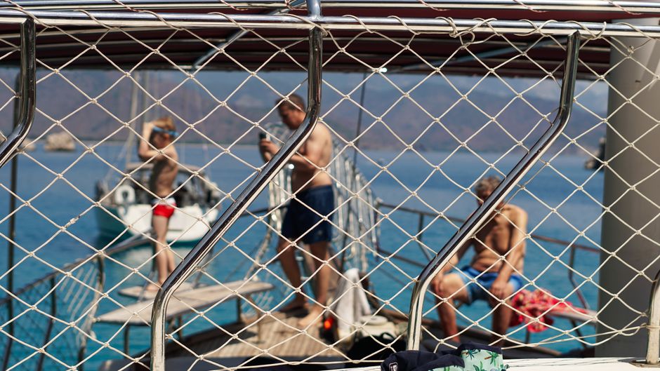 Men enjoying a sunny day on a yacht with clear ocean view through netting.