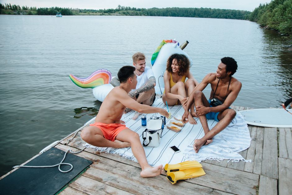 A joyful group of friends having a picnic on a lakeside dock during a sunny summer day.